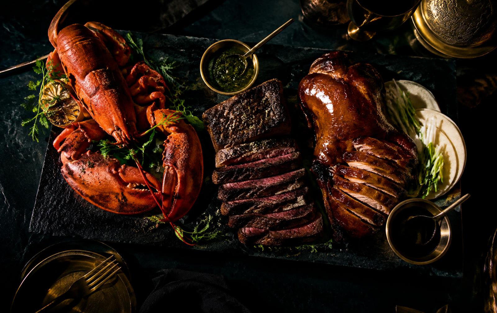 Whole lobster, sliced steak and Peking duck on a slate platter